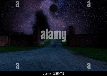 Tor und Zufahrtsstraße zur Residenz in der Nacht, in Dunkelheit gehüllt. In der Mitte des Rahmens absorbiert ein schwarzer Himmelskörper kosmische Materie. Stockfoto