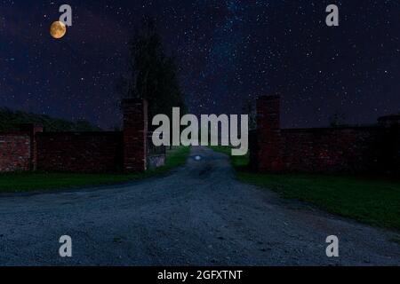 Tor und Zufahrtsstraße zur Residenz in der Nacht, in Dunkelheit gehüllt. Am Himmel sieht man den Mond zur Seite. Stockfoto