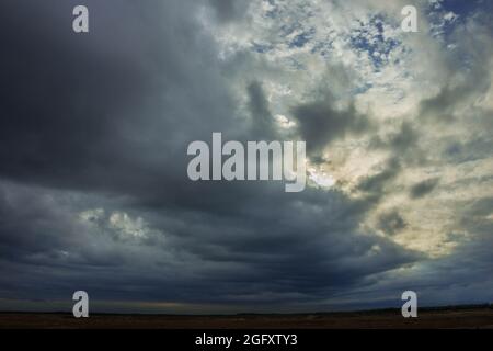 Eine weite Ebene, die mit Ackerfeldern und Wiesen bedeckt ist. Der Himmel ist bedeckt, bedeckt mit dunklen, ehrfurchtgebietenden Wolken, die den bevorstehenden Regenguss ankündigen. Stockfoto