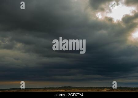 Eine weite Ebene, die mit Ackerfeldern und Wiesen bedeckt ist. Der Himmel ist bedeckt, bedeckt mit dunklen, ehrfurchtgebietenden Wolken, die den bevorstehenden Regenguss ankündigen. Stockfoto