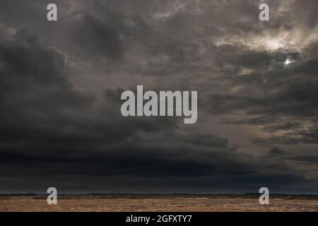 Eine weite Ebene, die mit Ackerfeldern und Wiesen bedeckt ist. Der Himmel ist bedeckt, bedeckt mit dunklen, ehrfurchtgebietenden Wolken, die den bevorstehenden Regenguss ankündigen. Stockfoto