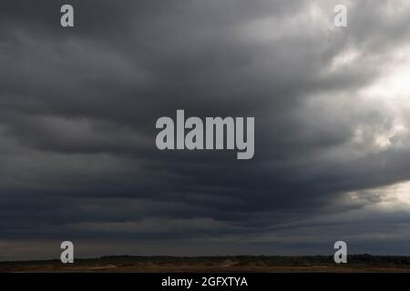 Eine weite Ebene, die mit Ackerfeldern und Wiesen bedeckt ist. Der Himmel ist bedeckt, bedeckt mit dunklen, ehrfurchtgebietenden Wolken, die den bevorstehenden Regenguss ankündigen. Stockfoto