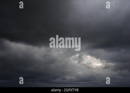 Eine weite Ebene, die mit Ackerfeldern und Wiesen bedeckt ist. Der Himmel ist bedeckt, bedeckt mit dunklen, ehrfurchtgebietenden Wolken, die den bevorstehenden Regenguss ankündigen. Stockfoto