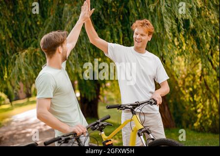 Ein fröhlicher, sportlicher junger Mann begrüßt seinen kumpel in einem Park Stockfoto