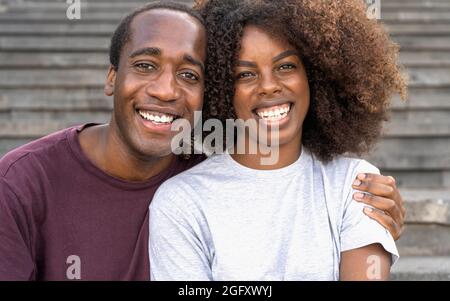 Glückliches afrikanisches Paar, das Spaß hat, in die Kamera zu lächeln, während es auf einer städtischen Treppe sitzt Stockfoto