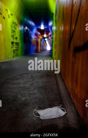 Verlassene gebrauchte Gesichtsmaske im U-Bahn-Tunnel mit Graffiti Stockfoto