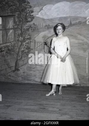 1957, historisch, eine Teenager-Darstellerin, die in der Pantomine auftaucht, Jack and the Beanstalk, die in ihrem Kostüm, einem langen Kleid und einem Zauberstab auf der Bühne steht, England, Großbritannien. Sie spielt den Charakter der Feenfrau. Jack and the Beanstalk, eine berühmte englische Volksgeschichte, ist eine uralte Fabel über einen armen Jungen, der, von seiner Mutter gesagt, die Kuh seiner Familie auf einem Markt zu verkaufen, sie stattdessen gegen fünf „magische“ Bohnen eintauscht, die zu einer aufrührerischen Bohnenstange wachsen, die in den Himmel steigt, Die Jack aufsteigt und Abenteuer hat. Stockfoto