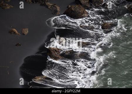 Schwarzer Basaltsand und Felsen an isländischer Küste Stockfoto