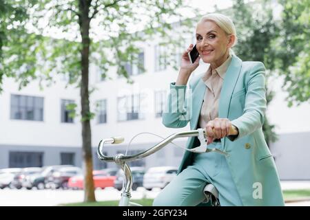 Ältere Geschäftsfrau, die im Freien auf dem Fahrrad sitzt und mit dem Mobiltelefon spricht Stockfoto