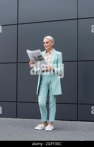 Leitende Geschäftsfrau liest Zeitung, während sie in der Nähe von Gebäuden im Freien steht Stockfoto