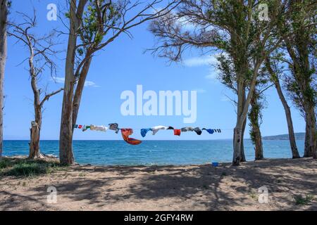Camper Kleidung trocknen auf einer Wäscheleine, aufgereiht zwischen Bäumen, neben dem Meer an einem Strand in Südgriechenland. Stockfoto