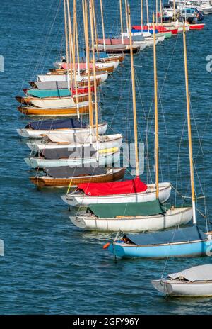 Kleine Yachten, die in einer Linie in lymington festgemacht sind, kleine Segeljollen, bunte Segelboote in einer Linie, kleine Segelyachten, die in Kurvenform festgemacht sind. Stockfoto