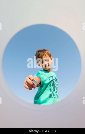 Kind legt einen Stapel in einen Recyclingbehälter, von innen gesehen, mit einem blauen Himmel im Hintergrund. Konzept von Recycling und Bildung in enviro Stockfoto