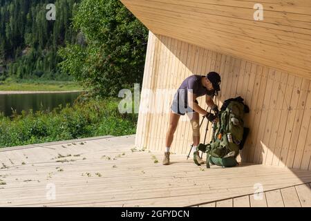 Region Perm, Russland - 13. August 2021: Wanderer nahm seinen Rucksack ab und ruht auf einer hölzernen Aussichtsplattform in einem Pavillon am Flussufer Stockfoto