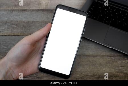 Nachbildung der Hand, die das Mobiltelefon auf dem Schreibtisch hält. Telefon Leerer Bildschirm Auf Holztisch, Mockup Phone. Stockfoto