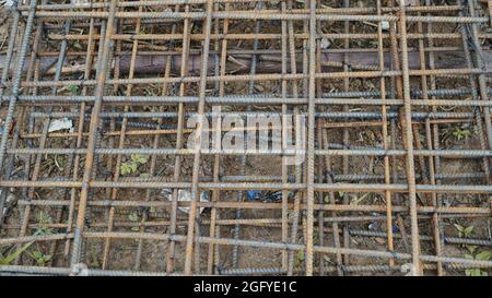 Das im Bau befindliche Gebäude wartet auf das Ausgießen von Betonplatten. Rostige Metallverdrahtung wird auf dem Boden des im Bau befindlichen Hauses verlegt. Stockfoto