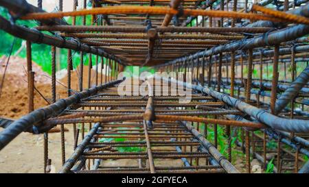 Das im Bau befindliche Gebäude wartet auf das Ausgießen von Betonplatten. Rostige Metallverdrahtung wird auf dem Boden des im Bau befindlichen Hauses verlegt. Stockfoto