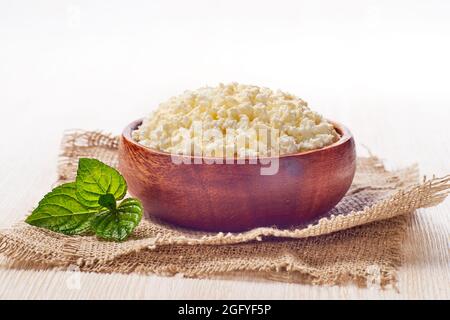 Schüssel mit Hüttenkäse auf Leinenserviette auf weißem Holzhintergrund Stockfoto