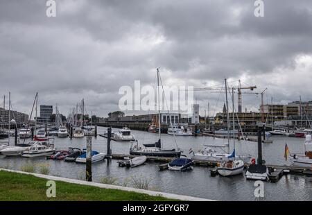 Zeebrugge Port, Belgien - 6. August 2021: Yachthafen mit vielen Vergnügungsbooten unter stark regnerischer Wolkenlandschaft. Weißer Uhrenturm und große Geschichte Stockfoto