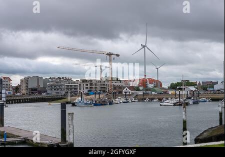 Zeebrugge Port, Belgien - 6. August 2021: Werfkaai Abschnitt des Yachthafens mit hohen Windmühlen und Baukräne im Rücken unter starker Regenwolke Stockfoto