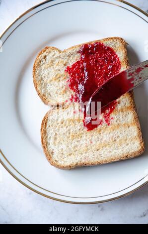 Jelly Jam aus roter Beere auf Toastbrot auf weißem und goldenem Teller verteilen Stockfoto