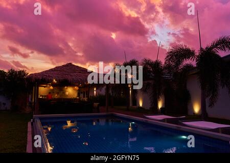 Ein sanfter Sonnenuntergang Himmel über einem reetgedeckten Bungalow. Ein exotisches Resort in den Tropen. Stockfoto