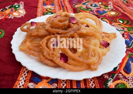 Beliebt und traditionell Süßes Gericht Jalebi oder Zulbia frittiert in Ghee mit Rosenblättern mit authentischen festlichen Hintergrund dekoriert Stockfoto