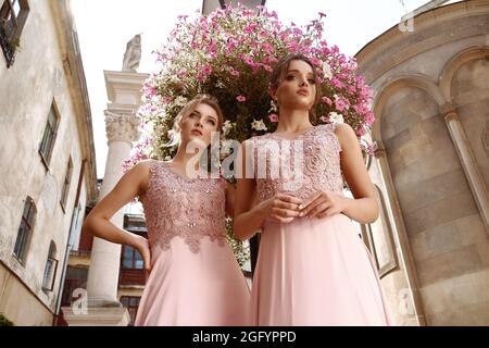 Low-Angle-Ansicht von zwei jungen europäischen Brautjungfern in rosa Kleidern Stockfoto