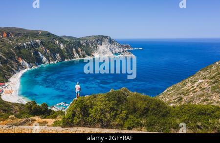 Panorama-Luftaufnahme eines Mannes, der auf einem Felsen mit einem aufregenden Gefühl der Freiheit steht und auf den Petani Beach blickt. Kefalonia ionische Insel, Griechenland Stockfoto