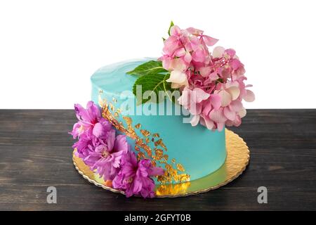 Ein schöner Concept Cake aus blauer Creme und Blumen. Auf einem Holztisch, auf weißem Hintergrund. Stockfoto