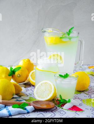 Krug aus Limonade mit gefülltem Maurer-Glas und Glas, umgeben von Zitronenscheiben, Eisminzlöffel aus Holz Stockfoto