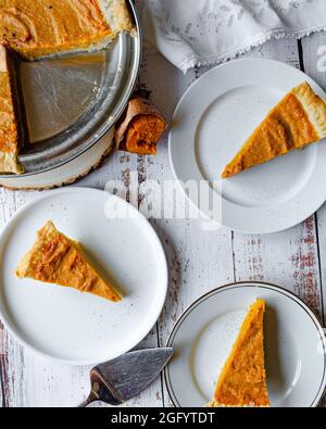 Süßkartoffelkuchen in Schale und Teller mit Scheiben auf weißem Tisch Stockfoto