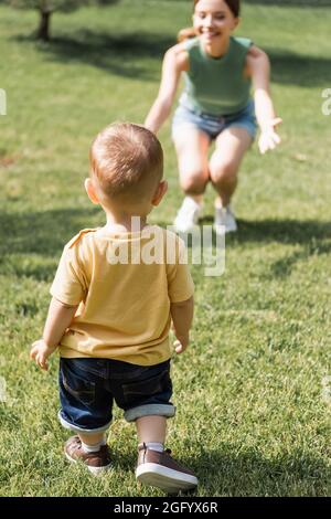 Rückansicht des Kleinkindes Jungen in der Nähe verschwommen fröhliche Mutter mit ausgestreckten Händen Stockfoto