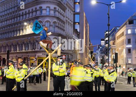 London, Großbritannien. 27th. August 2021. Extinction Rebellion (XR) und Tierrebellion Protestierende durchreisen den Londoner Finanzdistrikt , Quadratmeile, bis in die Nacht, besetzen die Kreuzung von Queen Victoria Street und Cannon Street, bis zur Bank of England, Gegen den globalen Klimawandel. Klettern Sie auf Bambusstrukturen, die mitten auf der Straße errichtet wurden, um gegen Investitionen in fossile Brennstoffe zu protestieren. Protestierende sitzen auf der Straße und protestieren. Quelle: Xiu Bao/Alamy Live News Stockfoto