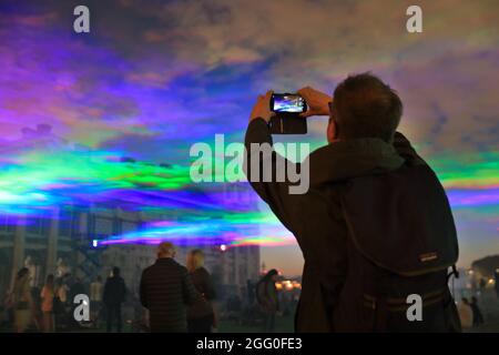 Greenwich, London, Großbritannien. August 2021. Die Menschen beobachten das Spektakel. An seiner offiziellen öffentlichen Startnacht beleuchtet „Borealis“ von Dan Archer den Himmel über dem Old Royal Naval College im Royal Borough of Greenwich. „Borealis“ ist eine faszinierende Nachbildung der Nordlichter am Himmel. Es ist Teil des jährlichen Greenwich and Docklands Festivals, das vom 27. August bis 11. September 2021 stattfindet. Kredit: Imageplotter/Alamy Live Nachrichten Stockfoto