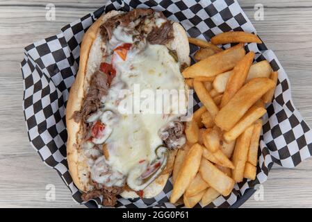 Blick von oben auf das offene Philly Cheesesteak-Sandwich, das in geschältem Käse überbacken ist, serviert mit Steak, pommes frites für eine appetitliche Mahlzeit. Stockfoto