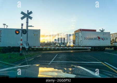 Tauranga Neuseeland - Januar 6 2016; Container im Zug passieren Bahnübergang, während die Schranke heruntergefahren ist und Autos warten. Stockfoto