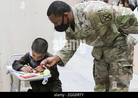 Ein Soldat der US-Armee und ein afghanischer Evakuierungsjunge färben sich im Lager Buehring, Kuwait, am 25. August 2021. Soldaten nahmen an Aktivitäten mit den Kindern Teil, während ihre Familien die Ankunftsverfahren in der Einrichtung durchliefen. (USA Armeefoto von Sgt. Marc Loi) Stockfoto