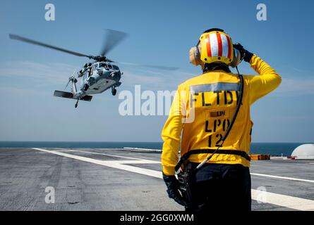 210826-N-LX838-1288 ATLANTIK (AUG 26, 2021) Aviation Boatswain's Mate (Handling) 1st Class Stephen Vaiza, der auf dem Flugzeugträger USS George H. W. Bush (CVN 77) dem Luftverkehrsministerium zugewiesene Flugdekor aus Socorro, New Mexico, sendet Signale an einen Sea Hawk-Hubschrauber der MH-60S, der dem Hubschrauber Sea Combat Squadron (HSC) 5 zugewiesen wurde, Das erste Flugzeug, das seit Beginn der Wartungszeit auf dem Flugdeck landet. Das Schiff wird im Atlantischen Ozean zur Unterstützung von Marineinteraktionen eingesetzt, um die maritime Stabilität und Sicherheit zu gewährleisten, um den Zugang zu gewährleisten, abschrecken aggres Stockfoto