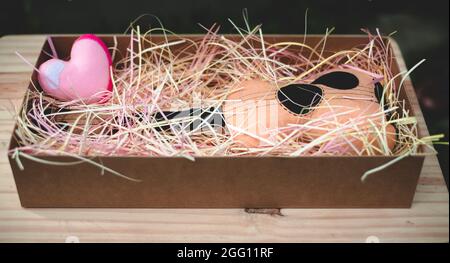 Spielzeug Plüsch Gitarre und ein rosa Herz in einer Geschenkbox mit bunten Papierstreifen gefüllt, Jahrestag Feier schöne Geschenkidee. Stockfoto