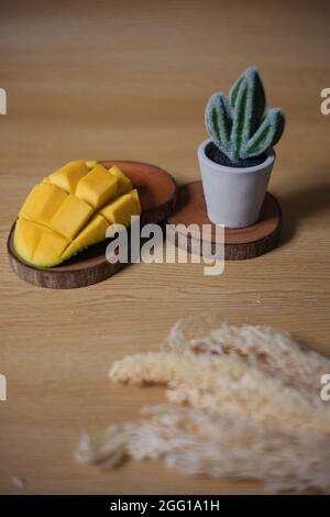 Mangostücke in Form einer blühenden Blume. Frische Früchte und niedliche Kakteen auf Holzgrund, Stockfoto