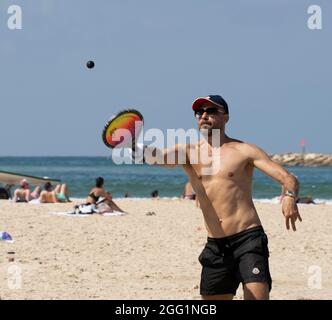 Tel Aviv, Israel - 15. August 2021: Ein junger Mann während eines matkot-Spiels am Strand von Tel Aviv, Israel, an einem klaren, sonnigen Tag. Stockfoto