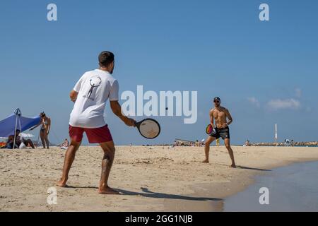 Tel Aviv, Israel - 15. August 2021: Zwei junge Männer spielen matkot an einem klaren, sonnigen Tag am Strand von Tel Aviv, Israel. Stockfoto