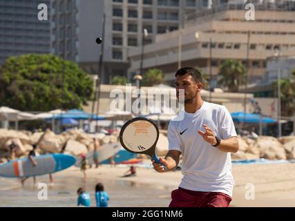 Tel Aviv, Israel - 15. August 2021: Ein junger Mann während eines matkot-Spiels am Strand von Tel Aviv, Israel, an einem klaren, sonnigen Tag. Stockfoto
