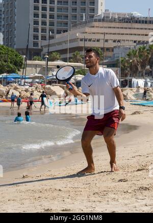 Tel Aviv, Israel - 15. August 2021: Ein junger Mann während eines matkot-Spiels am Strand von Tel Aviv, Israel, an einem klaren, sonnigen Tag. Stockfoto