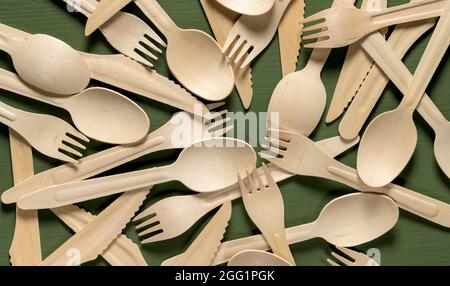 Einweg-Geschirr aus natürlichen Materialien. Stapel Holzlöffel, Gabel, Messer auf grünem Holztisch Stockfoto