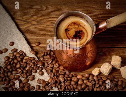 Turk mit frisch gebrühtem Kaffee auf Holzhintergrund Stockfoto
