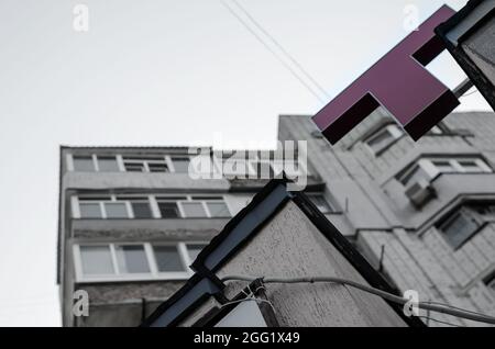 Red Capital T gegenüber dem grauen Himmel und den Apartments. Die Ecke des Gebäudes mit einem gewellten Elektrokanal im Vordergrund. Ansicht von unten Stockfoto