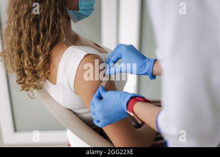 Ärztin in Schutzhandschuhen steckte Patchafter-Impfung in die Schulter. Covid 19-Impfung. Frauen erhalten Injektion in der Schulter. Impfstoff klinisch Stockfoto