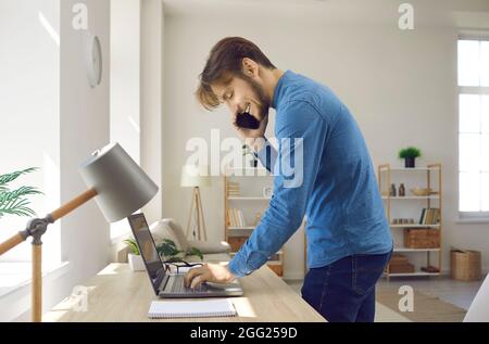 Freundlicher junger Geschäftsmann, der bei der Arbeit im Büro ein Geschäftsgespräch am Telefon führt. Stockfoto